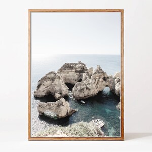 May include: A framed photograph of a rocky coastline with a turquoise ocean. The rocks have arches and caves, and there are small boats in the water.