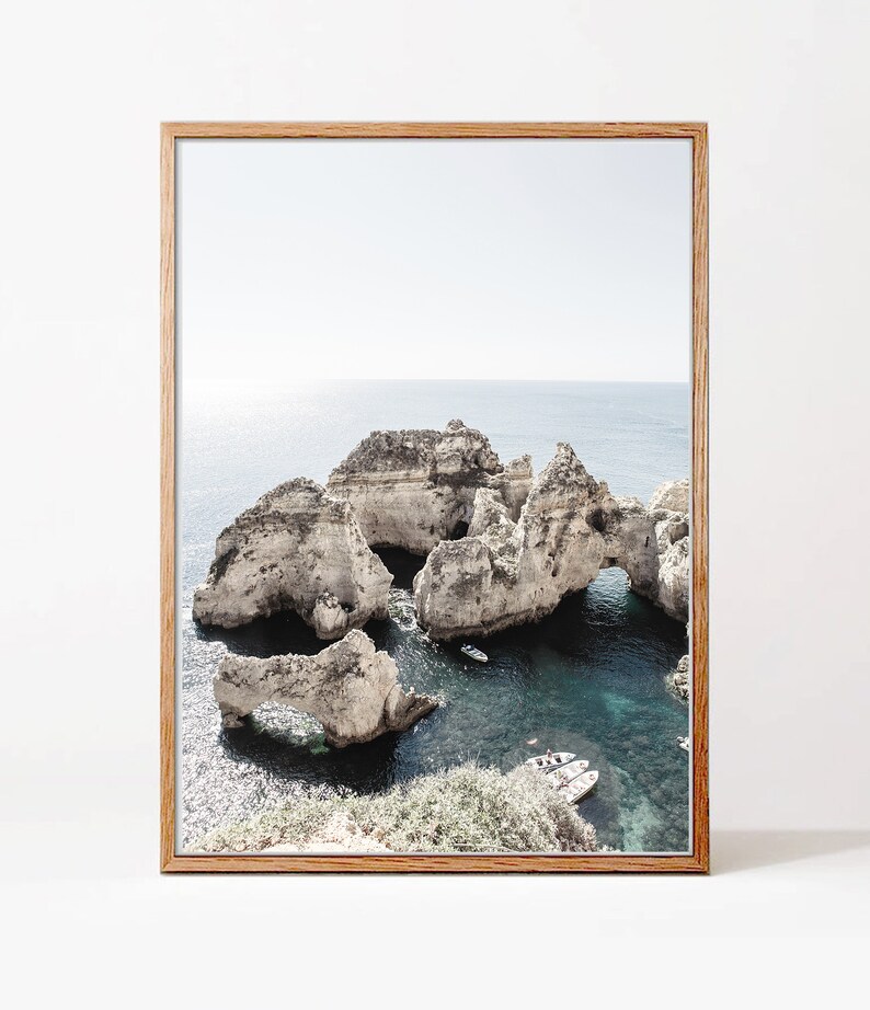May include: A framed photograph of a rocky coastline with a turquoise ocean. The rocks have arches and caves, and there are small boats in the water.