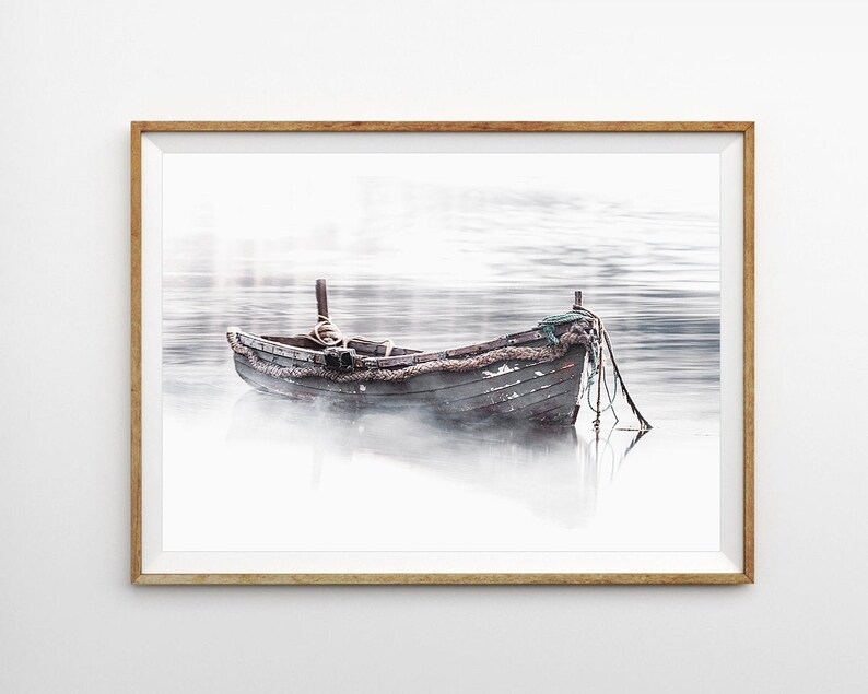 May include: A weathered wooden boat sits in a foggy, still body of water. The boat is tied to a dock with rope. The water is a light gray color and the fog is a white color.