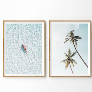 May include: Two framed art prints. One shows a person floating in clear turquoise water. The other depicts two tall palm trees against a light blue sky. Both prints are in wooden frames.