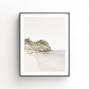 Puede incluir: Una fotograf&iacute;a enmarcada de una playa rocosa con una peque&ntilde;a isla en la distancia. La playa es de arena blanca y el agua es de color azul claro. El cielo es de color gris claro.
