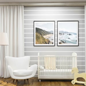 May include: A white crib with a white blanket and a wooden rocking horse in a nursery with white curtains and two framed landscape photographs of a beach.