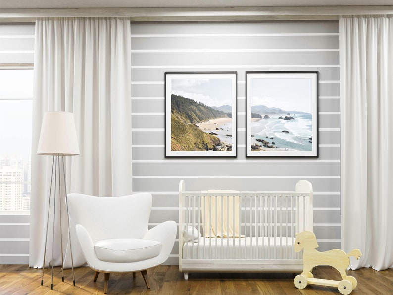 May include: A white crib with a white blanket and a wooden rocking horse in a nursery with white curtains and two framed landscape photographs of a beach.