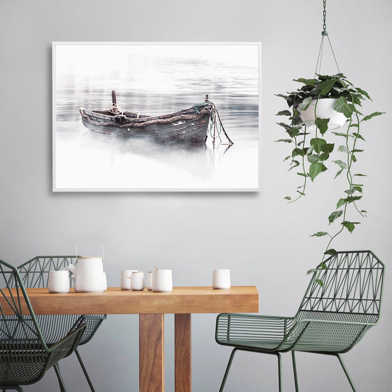 May include: A black and white photograph of a wooden boat on a foggy lake. The boat is weathered and has a rope attached to it. The photo is framed in a white frame.