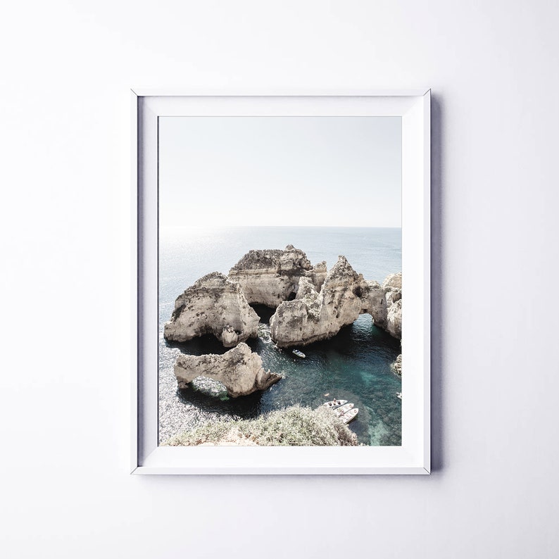 May include: A photograph of a rocky coastline with a turquoise blue ocean. The rocks have arches and caves, and there are small boats in the water.