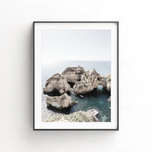May include: A photograph of a rocky coastline with a turquoise blue ocean. The rocks are white and have many caves and arches. There are small boats in the water.