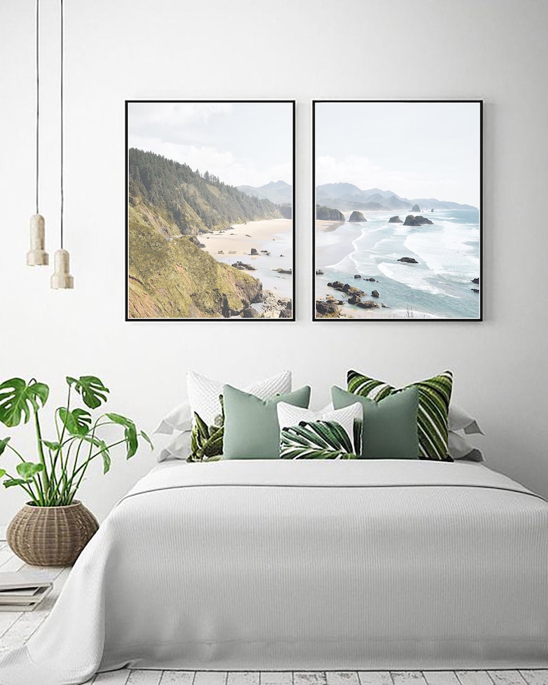 May include: Two framed landscape photographs of a beach with rocky cliffs and ocean waves. The photos are hung on a white wall above a white bed with green and white pillows.