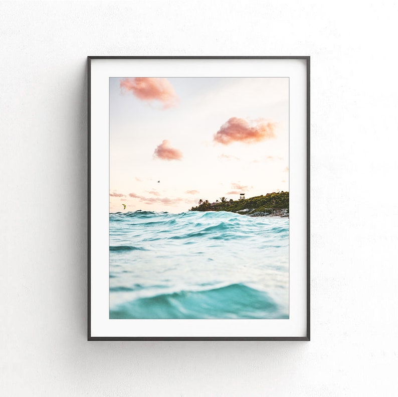 May include: A framed photograph of a turquoise ocean with waves crashing against the shore. The sky is a soft pink with fluffy clouds. A small island with green trees is visible in the distance.