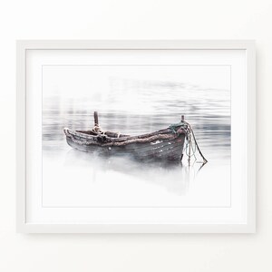 May include: A weathered wooden boat sits in a misty lake, with a rope and net trailing in the water.