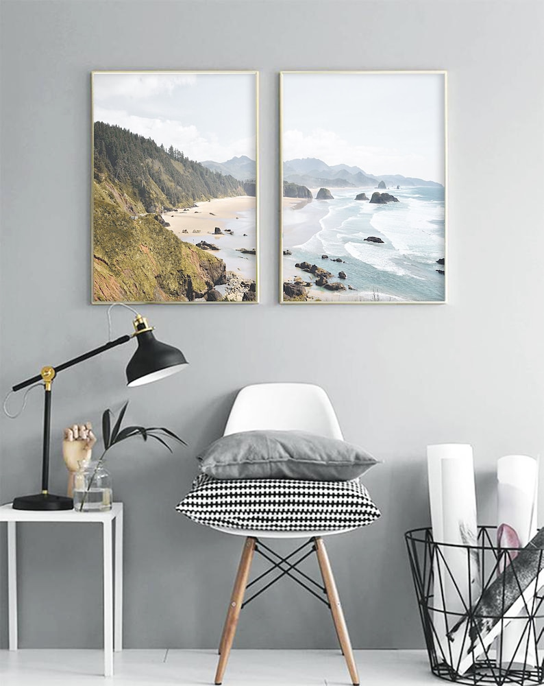 May include: Two framed landscape photographs of a beach with rocky cliffs and ocean waves. The photos are hung on a gray wall above a white chair with a black and white patterned cushion.