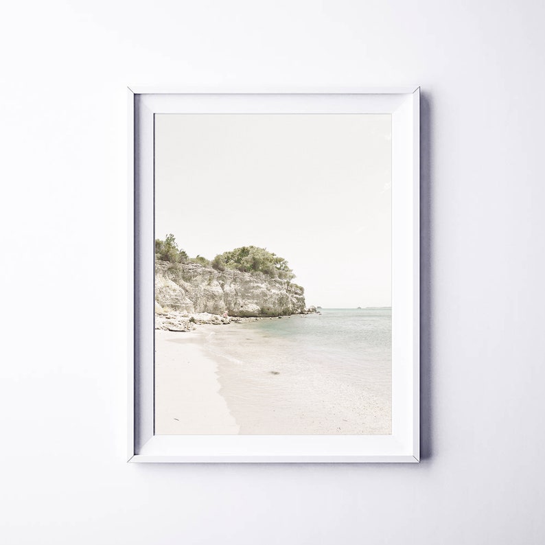 Puede incluir: Una fotograf&iacute;a enmarcada de una escena de playa con un acantilado rocoso y &aacute;rboles verdes en el fondo. El agua es de color azul claro y la arena es blanca.