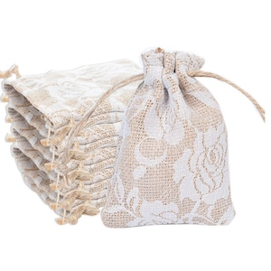 May include: A stack of small, white and beige burlap drawstring bags with a floral lace pattern. The bags are ideal for packaging small gifts or favours.