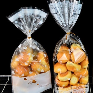 May include: Two clear plastic bags with white heart and swirl designs. The bags are filled with small, round, golden brown pastries. The text "The occasion" is printed on the bottom of one bag.