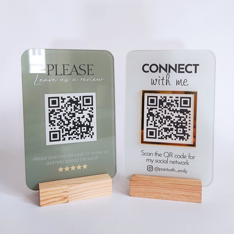 May include: Two acrylic signs with QR codes and wooden stands. The left sign is green and says "PLEASE Leave us a review" with a five-star rating. The right sign is white and says "CONNECT with me" with the text "Scan the QR code for my social network @paintwith_emily".