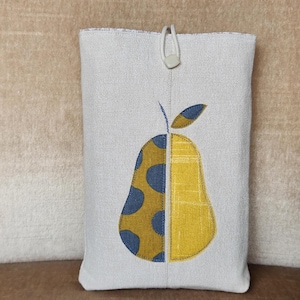 Könnte beinhalten: Eine rechteckige, cremefarbene Stoffhülle mit einem Birnenmuster. Die Birne ist vertikal geteilt, eine Seite mit blauen Punkten auf gelbem Grund und die andere Seite gelb. Oben befindet sich ein weißer Schlaufen- und Kordelverschluss.