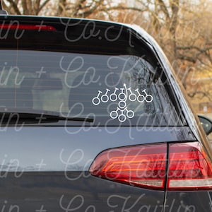 May include: A white vinyl decal of a bicycle chain design is affixed to the rear window of a dark gray car. The decal is a series of interconnected circles and arrows, suggesting a cycling theme.