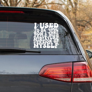 May include: A white vinyl decal on a car's rear window. The decal reads, "I USED TO BE COOL. NOW I JUST ARGUE WITH MINIATURE VERSION OF MYSELF" in a retro font. The car is dark gray.