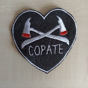 Puede incluir: Parche negro en forma de coraz&oacute;n con hachas cruzadas bordadas en blanco y la palabra "COPATE" en blanco.