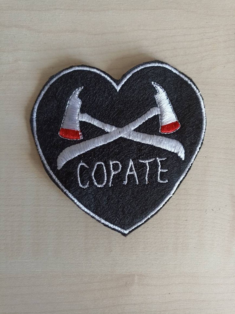 Puede incluir: Parche negro en forma de coraz&oacute;n con hachas cruzadas bordadas en blanco y la palabra "COPATE" en blanco.