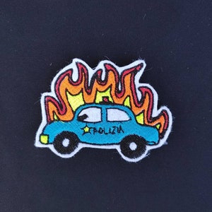 Può includere: Un'auto della polizia di cartone animato blu e bianca con una stella gialla sul lato è avvolta dalle fiamme. L'auto ha la scritta "POLIZIA" sul lato.