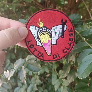 Può includere: Toppa ricamata rossa con un uccello dei cartoni animati che indossa occhiali protettivi e tiene una chiave inglese. Il testo "LOTTA DI CLASSE" è scritto intorno all'uccello.