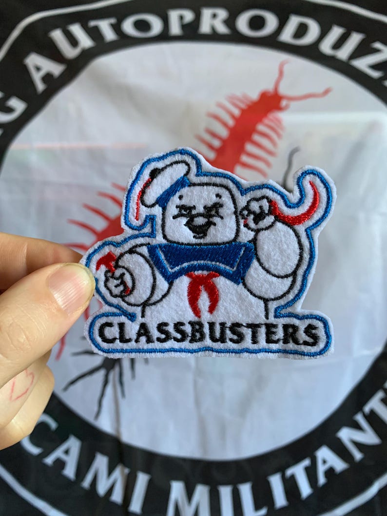 Pu&ograve; includere: Toppa ricamata con un personaggio dei cartoni animati in tenuta da marinaio, con la scritta "CLASSBUSTERS". Il personaggio &egrave; bianco con dettagli blu e rossi. Lo sfondo include testo e un'illustrazione rossa.