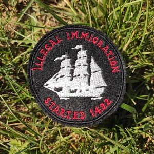 Può includere: Toppa rotonda nera con testo rosso "ILLEGAL IMMIGRATION STARTED 1492". Una nave a vela bianca è al centro. La toppa è su erba verde.
