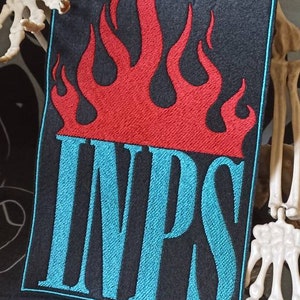 Può includere: Una toppa ricamata nera con un disegno di fiamma rossa e la parola "INPS" in lettere blu turchese.