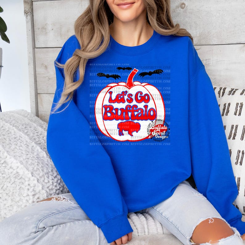 May include: A royal blue sweatshirt with a white pumpkin graphic. The pumpkin has the text "Let's Go Buffalo" in red and blue lettering. The graphic also includes a small buffalo silhouette and the text "Buffalo Spirit Designs".