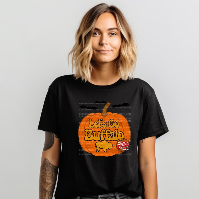 May include: Black t-shirt with a graphic of an orange pumpkin with the text "Let's Go Buffalo" and a buffalo silhouette. The text "Buffalo Spirit Designs" is also included.