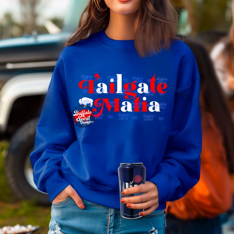 May include: Royal blue sweatshirt with the text "Tailgate Mafia" in red and white. The sweatshirt also features a buffalo graphic and the words "Buffalo Spirit Designs". A person is holding a can of beer.