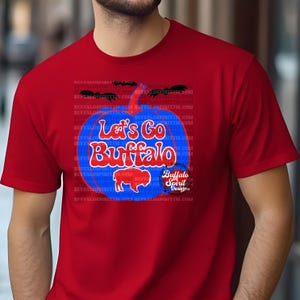 May include: Red t-shirt with a blue and red pumpkin design. The pumpkin has the text "Let's Go Buffalo" inside. A small buffalo silhouette is below the text. The text "Buffalo Spirit Designs" is in a circle below the pumpkin.