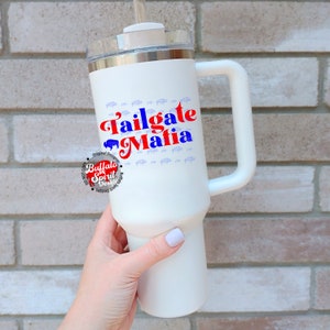 May include: White insulated tumbler with a handle, featuring the text "Tailgate Mafia" in red and blue. The design includes a buffalo graphic and small buffalo silhouettes. The tumbler has a clear lid and a straw.
