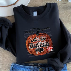 May include: Black sweatshirt with a glittery orange pumpkin design. The pumpkin has the text "Let's Go Buffalo" on it. The text "Buffalo Spirit Designs" is also on the sweatshirt.