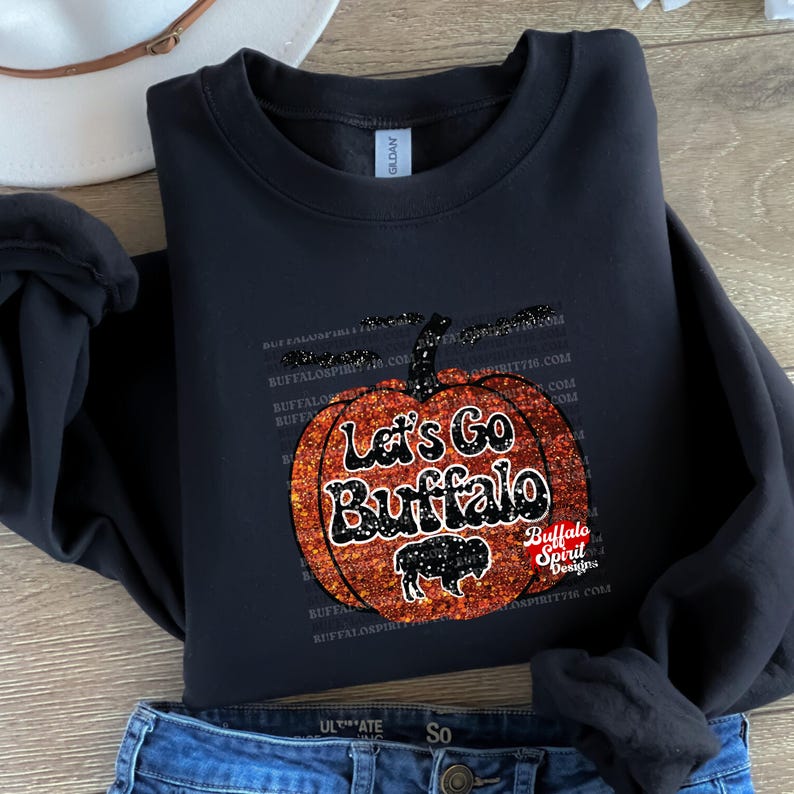 May include: Black sweatshirt with a glittery orange pumpkin design. The pumpkin has the text "Let's Go Buffalo" on it. The text "Buffalo Spirit Designs" is also on the sweatshirt.