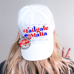 May include: White baseball cap featuring the text "Tailgate Mafia" in red and blue, with a buffalo graphic. The cap has a pattern of small buffalo silhouettes. The "Buffalo Spirit Designs" logo is visible on the side.