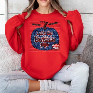 May include: Red sweatshirt with a blue and red glitter pumpkin with the text "Let's Go Buffalo" and a buffalo silhouette. The text "Buffalo Spirit Designs" is below the pumpkin.