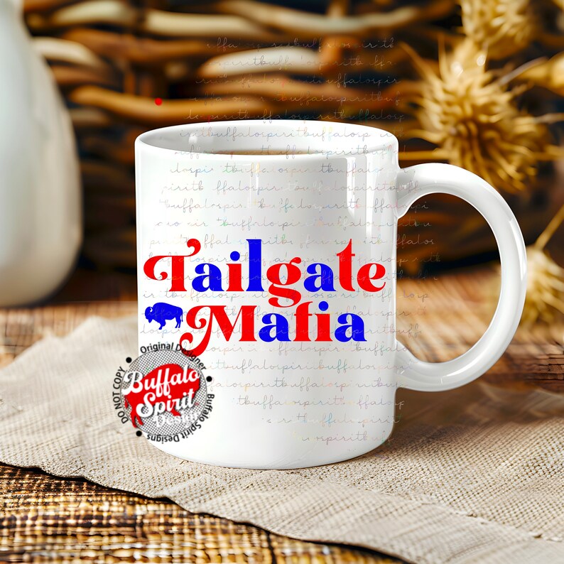 May include: White ceramic coffee mug with the words "Tailgate Mafia" in red and blue, with a buffalo graphic. The mug has a large handle and is on a wooden surface.