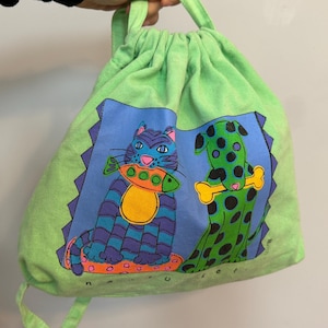 May include: A green drawstring bag with a cat and dog design. The cat is blue and purple with orange stripes and is holding a fish. The dog is green with black spots and is holding a bone.