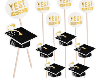 May include: Six white cupcake toppers with gold foil text that reads "YES! YOU DID IT" and six black graduation caps with gold accents on wooden sticks.