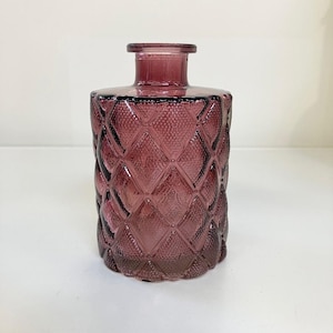 Könnte beinhalten: Eine violette Glasflasche mit einem Diamantenmuster. Die Flasche hat einen weiten Mund und einen kurzen Hals.