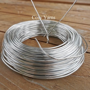 May include: A roll of silver-colored wire wrapped around a heart-shaped wire frame. The wire is labeled "Cosy Yarns".