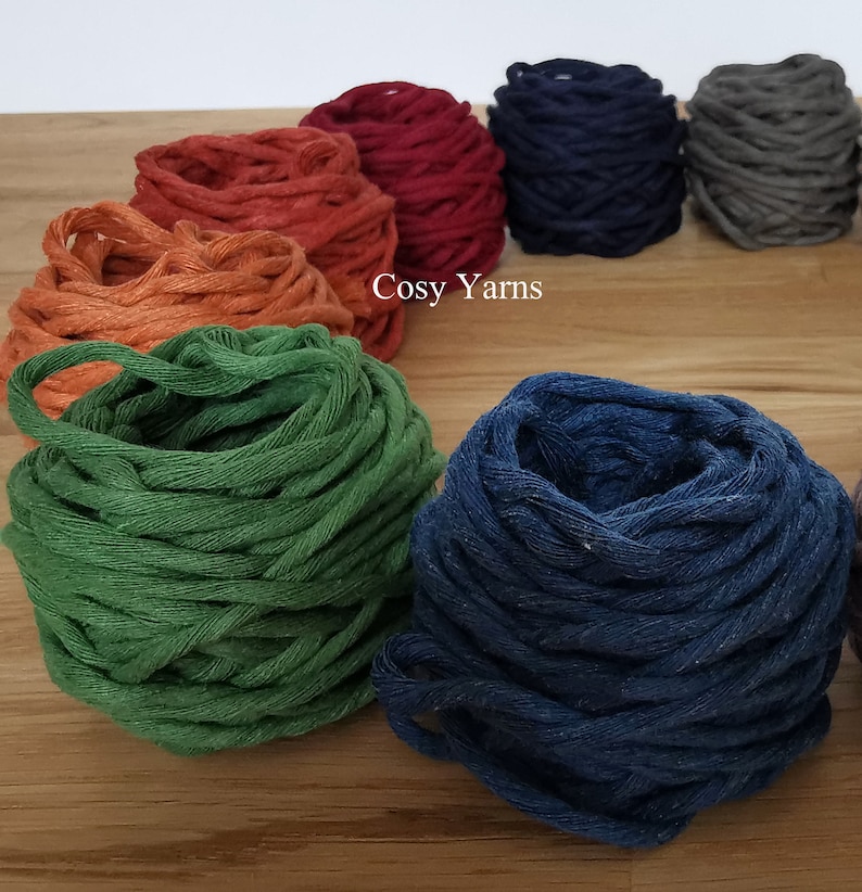 May include: Close-up of eight balls of yarn in various colors, including orange, red, blue, gray, and green. The yarn is arranged in a circle on a wooden surface. The text "Cosy Yarns" is visible in the center of the image.