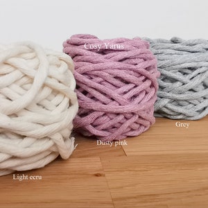 May include: Four balls of yarn in different colors: light ecru, dusty pink, grey, and petrol blue. The yarn is labeled "Cosy Yarns".