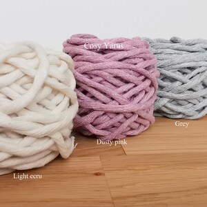 K&ouml;nnte beinhalten: Vier Kn&auml;uel Garn in verschiedenen Farben: helles Ecru, staubiges Rosa, Grau und Petrolblau. Das Garn ist mit "Cosy Yarns" gekennzeichnet.