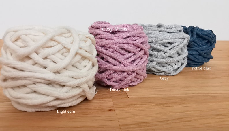 K&ouml;nnte beinhalten: Vier Kn&auml;uel Garn in verschiedenen Farben: helles Ecru, staubiges Rosa, Grau und Petrolblau. Das Garn ist mit "Cosy Yarns" gekennzeichnet.