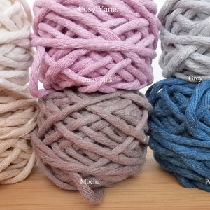 May include: Six spools of cotton yarn in various colors, including light ecru, sand beige, dusty pink, mocha, grey, and petrol blue. The spools are arranged in two rows of three, with the text "Cosy Yarns" printed above the top row.