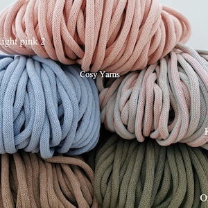 May include: Close-up of several skeins of chunky yarn in various colors, including light pink, blue, mocha, and oregano. The yarn is labeled "Light pink 2", "Blue", "Mocha", "Oregano", and "Rainbow". The text "Cosy Yarns" is also visible.