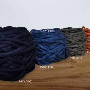 K&ouml;nnte beinhalten: Vier Kn&auml;uel Garn in verschiedenen Farben: Dunkelblau, Petrolblau, Dunkeloliv und Stauborange. Das Garn ist mit "Cosy Yarns" gekennzeichnet.