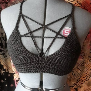 Pode incluir: Bralette de crochê preto com um design de pentagrama. A bralette está em um manequim e tem alças ajustáveis.